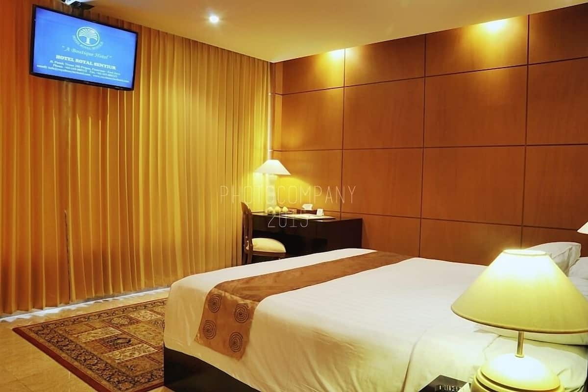 Quarto de hotel com uma cama grande, uma escrivaninha com luminária, televisão na parede e painel de parede de madeira.