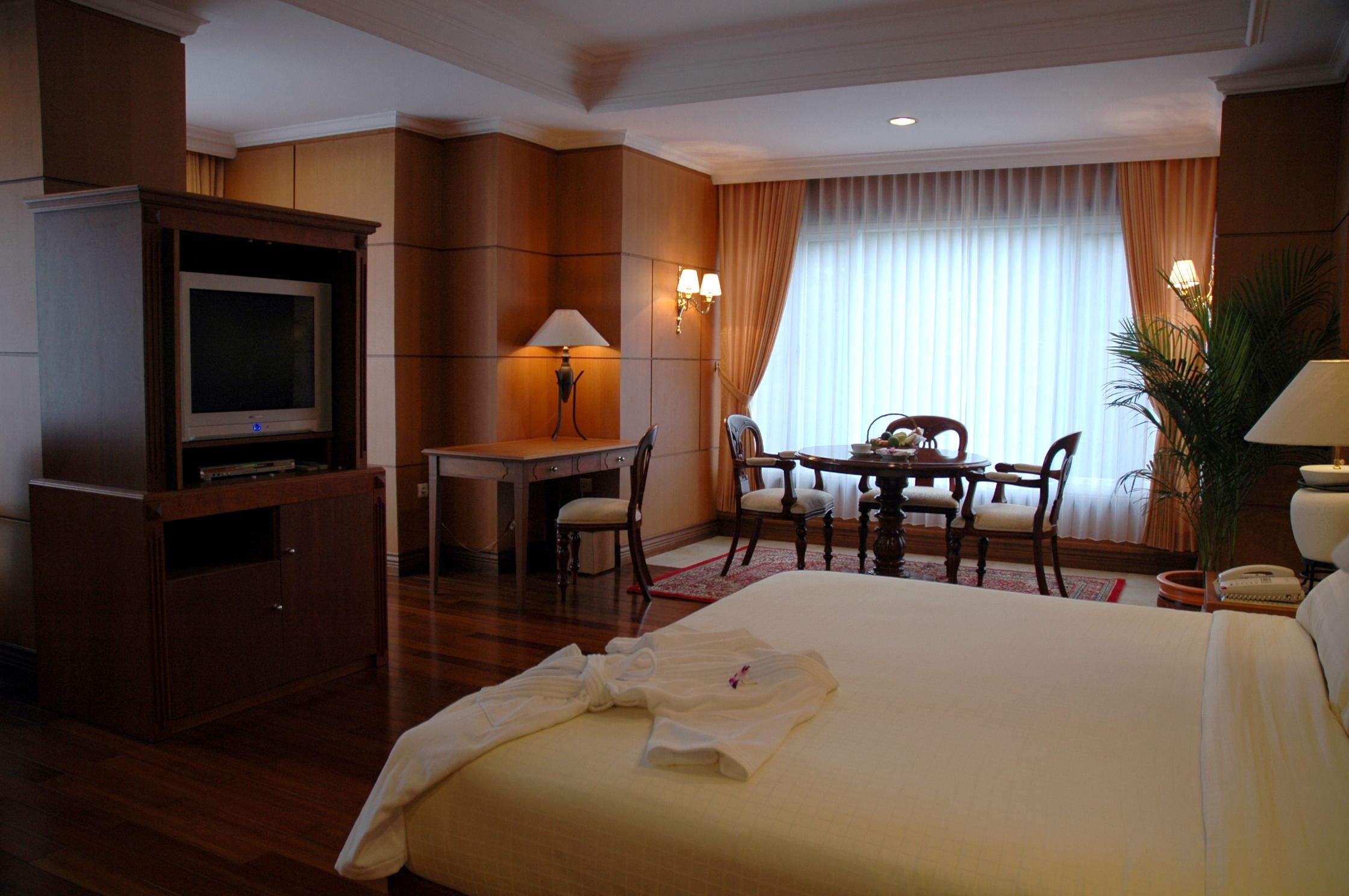 A hotel room with a bed, a desk, a chair, a television, and a lamp.
