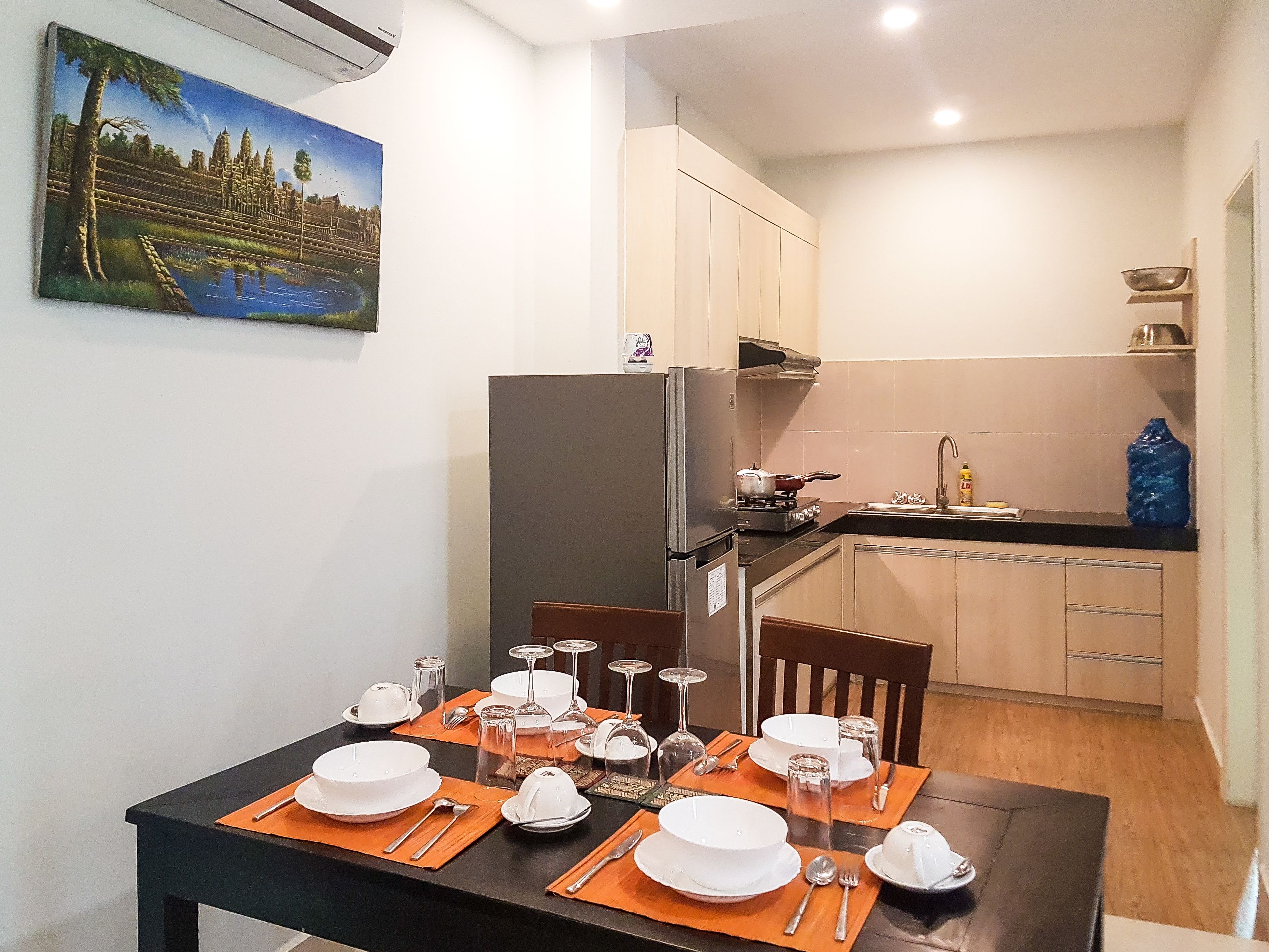 A compact kitchen with a refrigerator, stove, and sink. A dining table is set with plates, glasses, and cutlery.