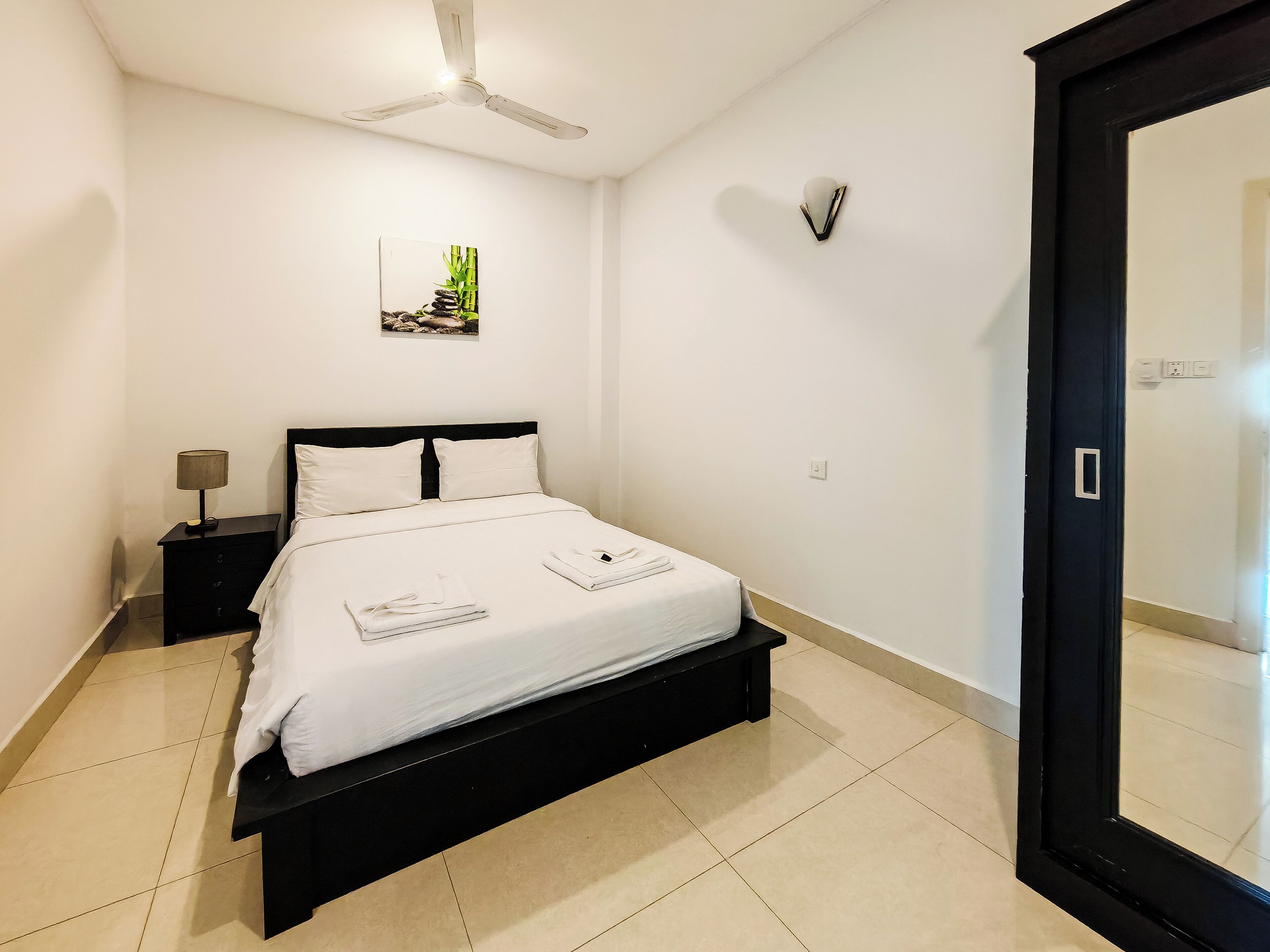 A neatly made bed with white linens, a black headboard, and a nightstand with a lamp.