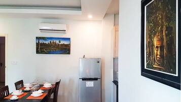A dining area with a table set for four, a refrigerator, and a Buddha statue on the wall.