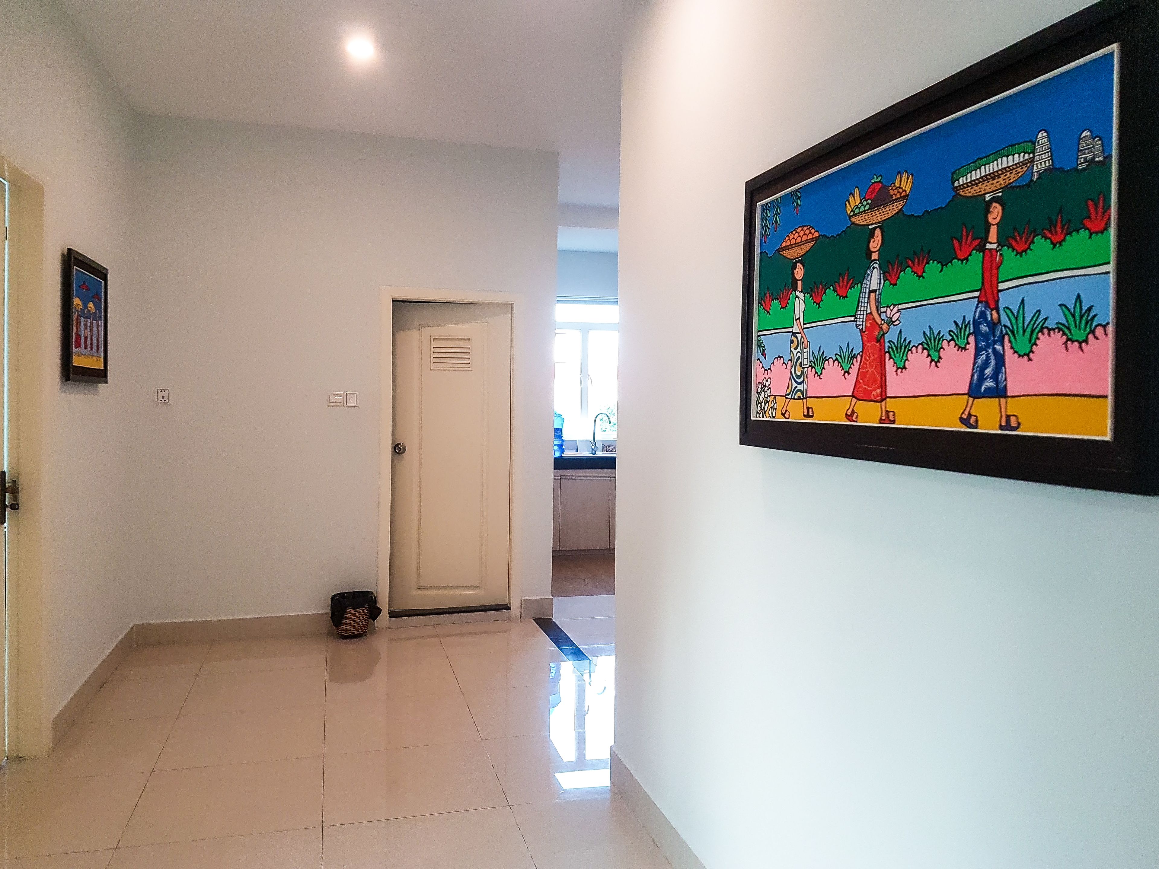 Un couloir avec un sol carrelé, une porte et un tableau encadré accroché au mur.