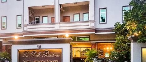 Un hotel de varios pisos con un letrero que indica La Belle Residence, ofreciendo apartamentos con servicios y un restaurante.