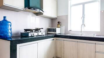 A kitchen with white cabinets, a black countertop, a stove, a microwave, a sink, and a large blue water dispenser.