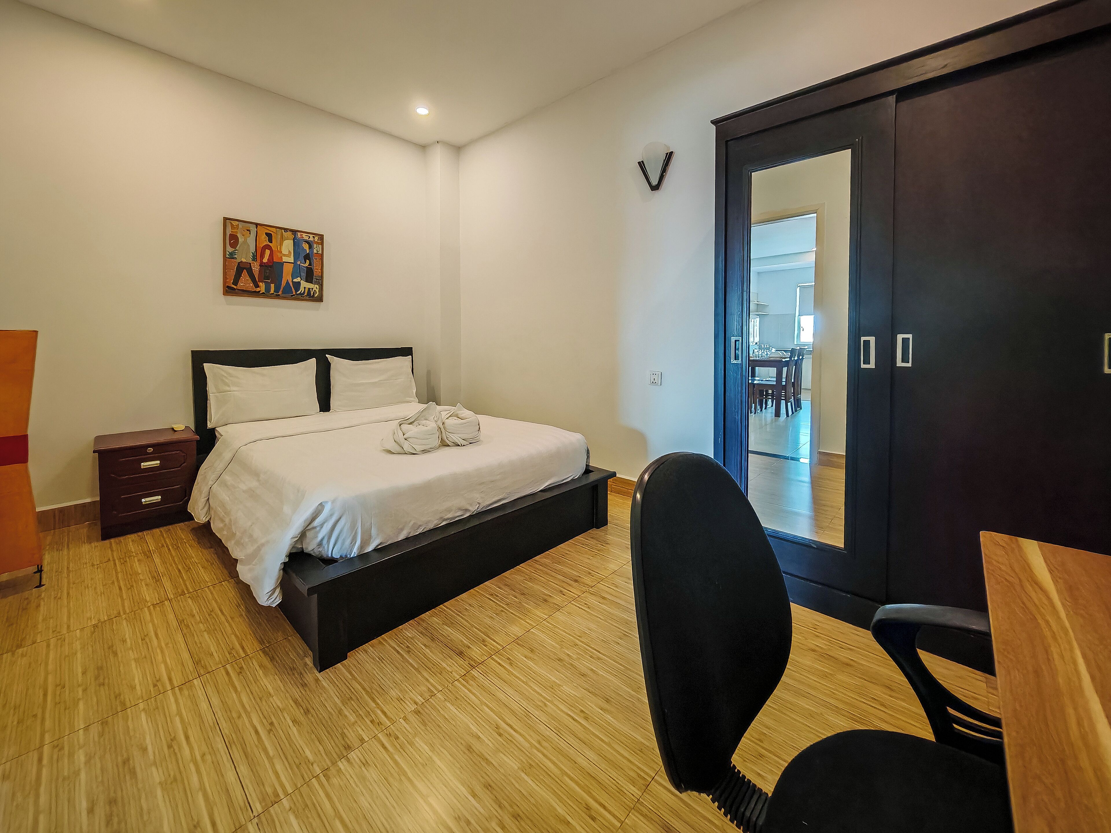 A bedroom with a bed, bedside tables, a desk, a chair, a wardrobe, and a painting on the wall.