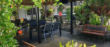 An outdoor seating area with a covered patio, a table with chairs, and a bench.