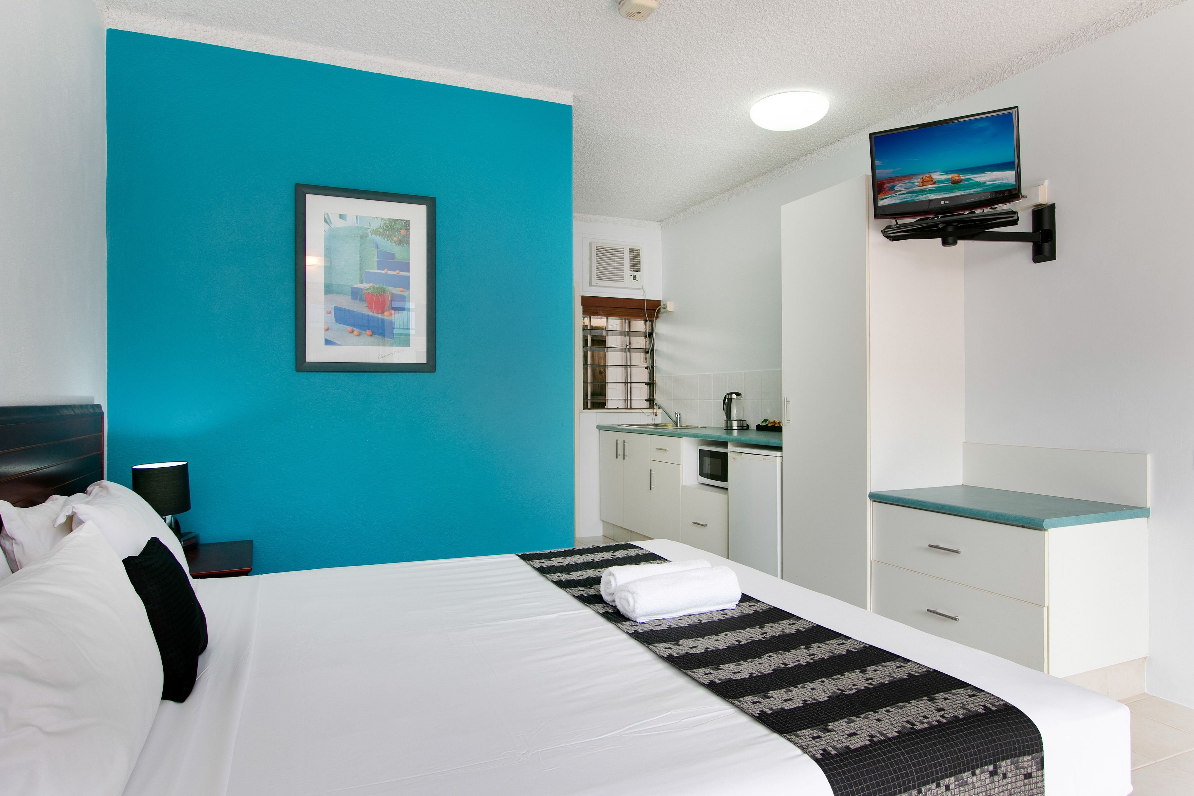 Una habitación de hotel con cama, escritorio, televisión y zona de cocina.