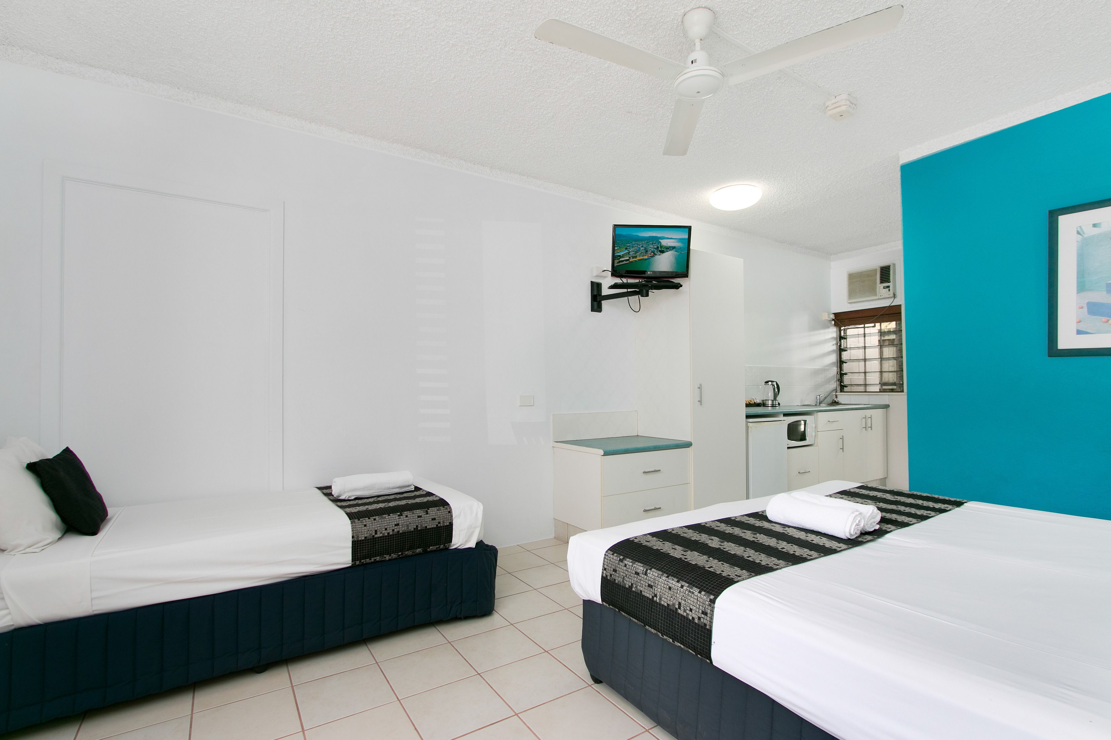 Habitación de hotel con dos camas, televisión, una kitchenette pequeña y baño.