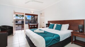 A hotel room with a large bed, a desk, a chair, and a balcony with a view of palm trees. - Cairns City Palms (Cairns North)