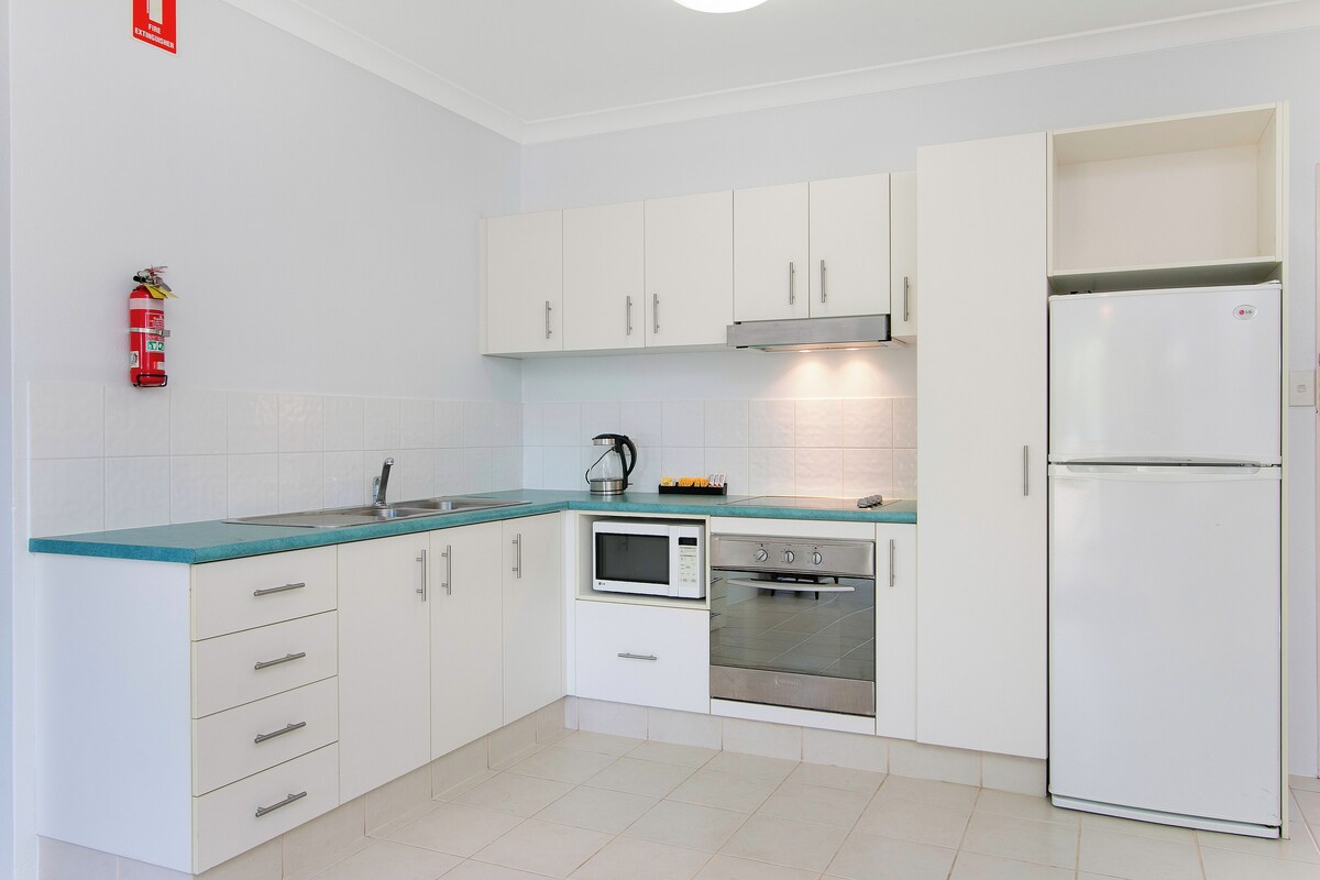 A modern kitchen with white cabinets, a stainless steel refrigerator, a microwave, and an oven.
