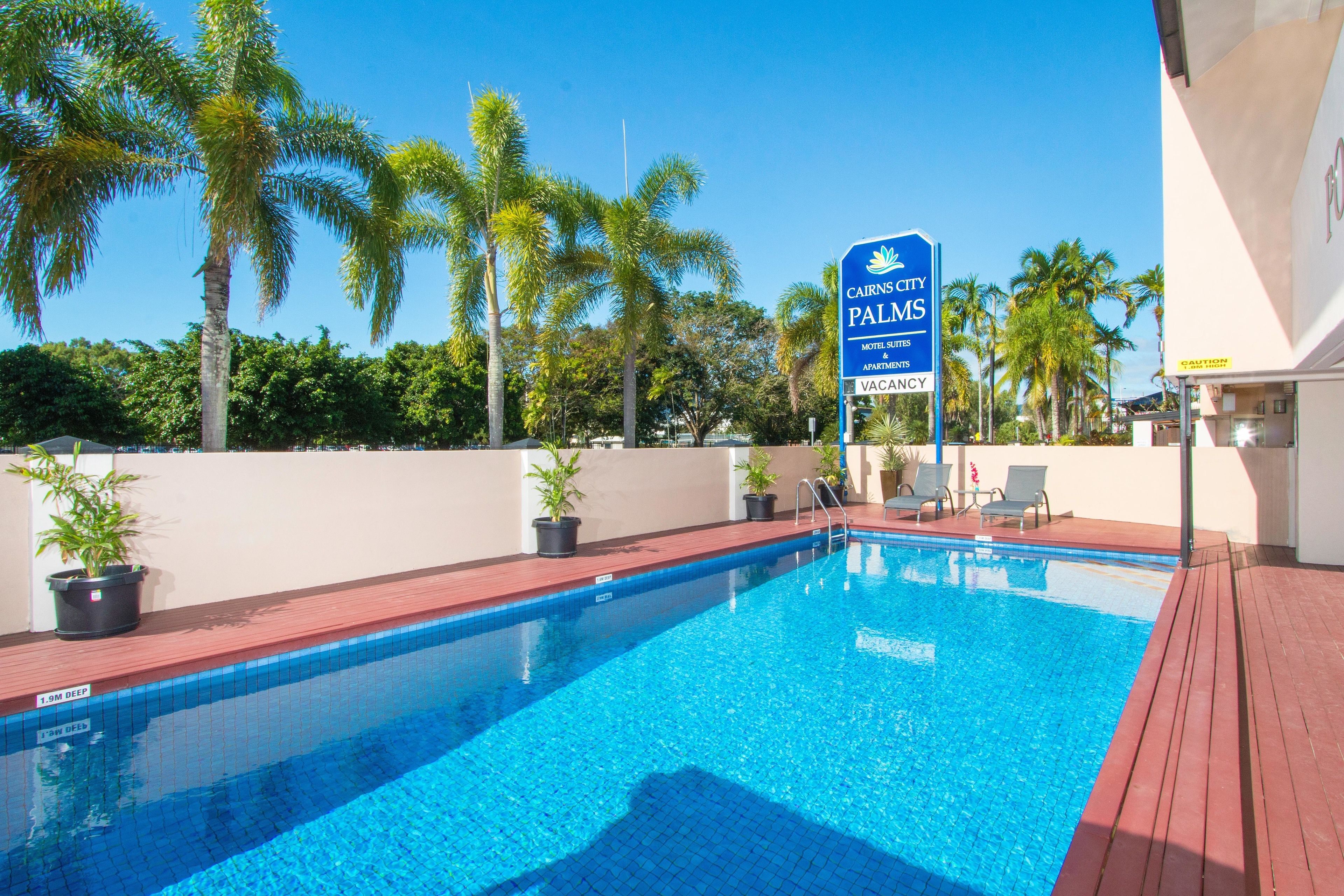 A swimming pool with a sign for Cairns City Palms Motel, Suites & Apartments.