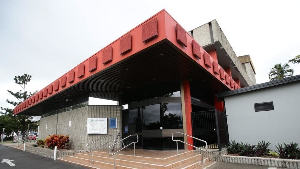 A modern building with a red and grey facade, a covered entrance with steps, and a small adjacent structure.