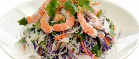 A plate of shrimp salad with shredded cabbage and carrots.