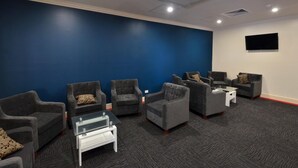 A room with a blue wall, grey armchairs, a white coffee table, and a flat-screen TV mounted on the wall. - Parklane Motel Murray Bridge (Murray Bridge)