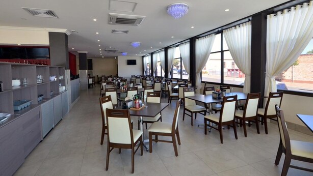 A spacious restaurant with multiple tables and chairs, a kitchen area on the left, and large windows with curtains. - Parklane Motel Murray Bridge (Murray Bridge)