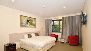 A hotel room with a large bed, a painting on the wall, a window with curtains, a TV mounted on the wall, and a red chair. - Parklane Motel Murray Bridge (Murray Bridge)