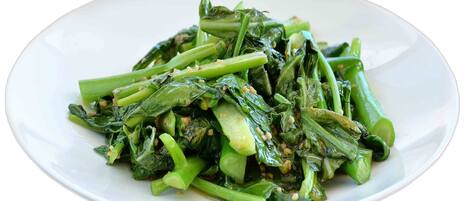 A white plate with cooked green leafy vegetables.