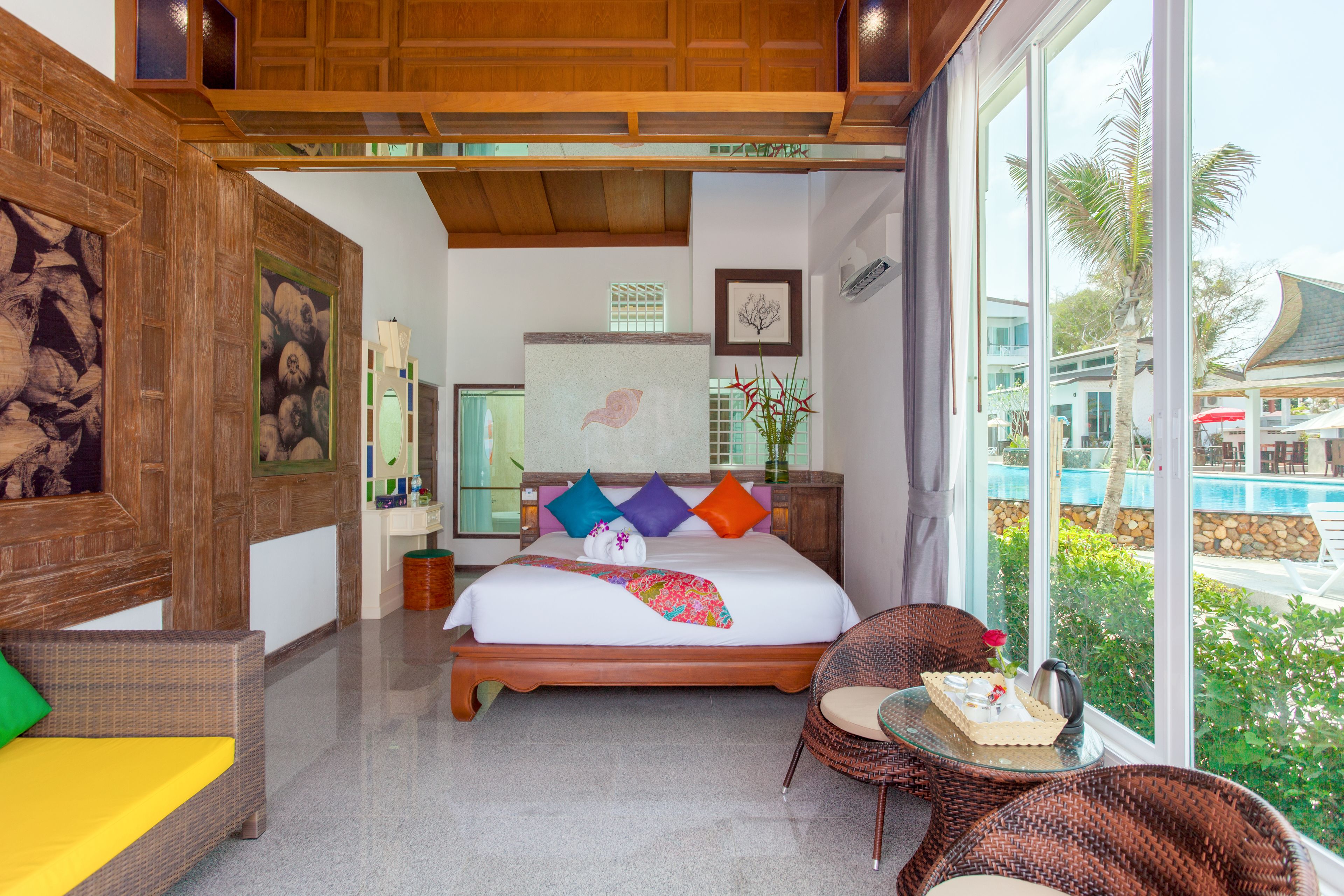 A hotel room with a large bed, a view of the pool, and a wicker chair by the window.