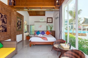 A hotel room with a large bed, a view of the pool, and a wicker chair by the window.