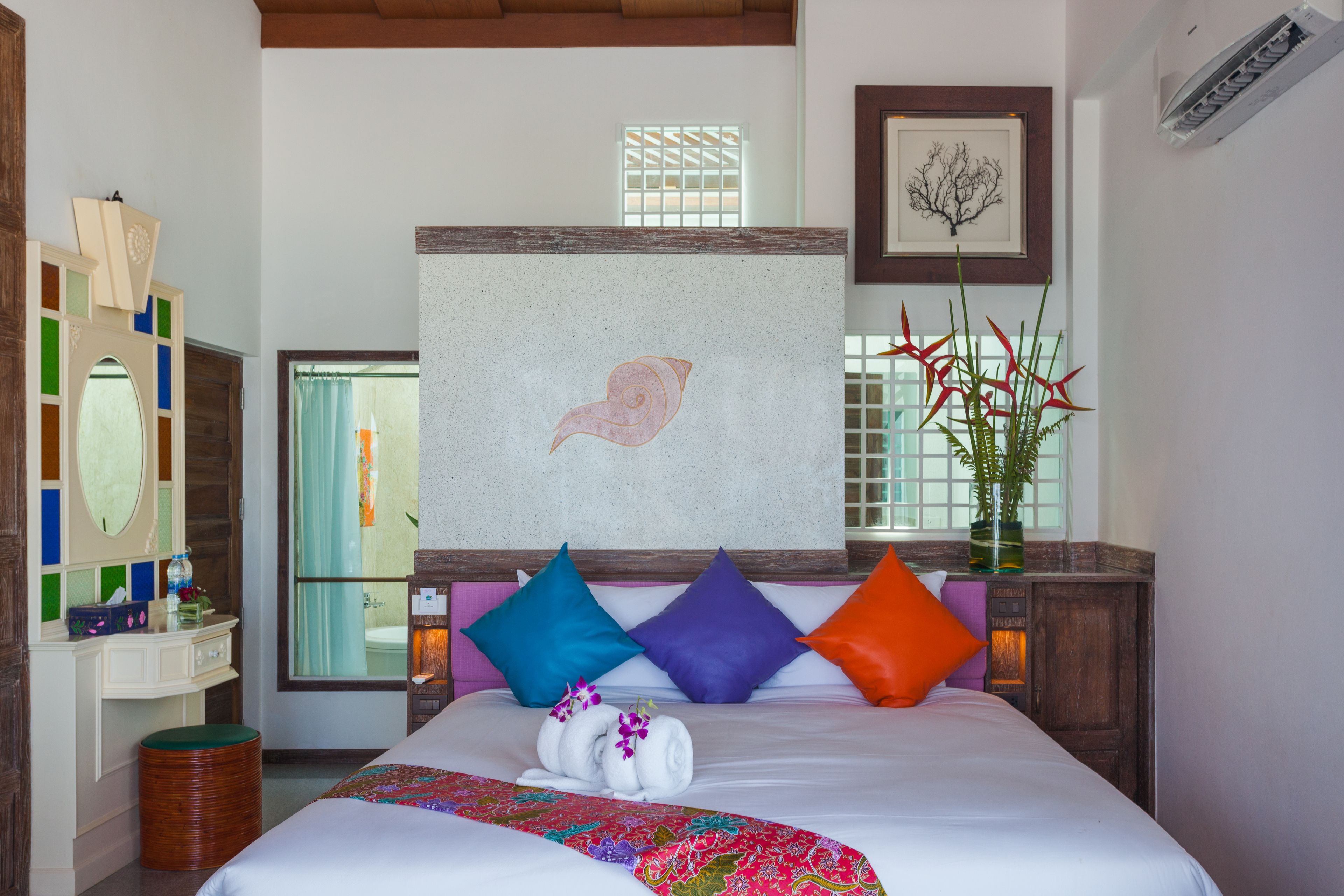 A hotel room with a large bed, colorful pillows, a decorative wall, and a window with a view.