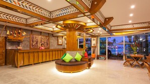 Eine Lobby mit Holzbeschreibungspult, einer zentralen Sitzecke mit Kissen und Blick ins Freie.
