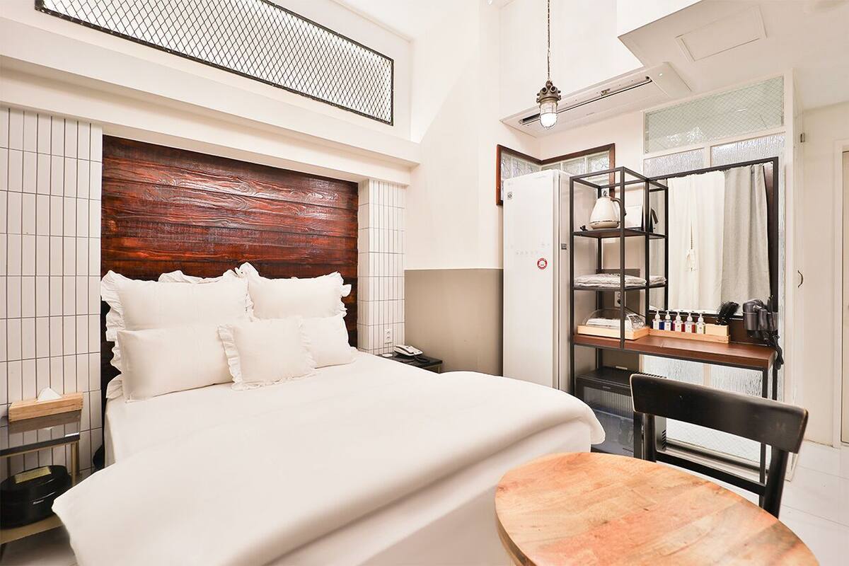 Quarto de hotel moderno com uma cama grande, cabeceira de madeira, escrivaninha com cadeira e janela com vista.