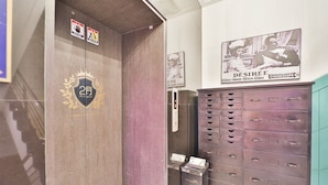 Een lift met een logo en een bord dat een verblijf van twee maanden aangeeft. Naast de lift bevindt zich een muur met een poster en een metalen berging.