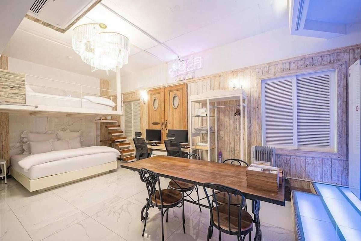 Un dormitorio con literas, una zona de comedor con una mesa y sillas de madera, y una araña.