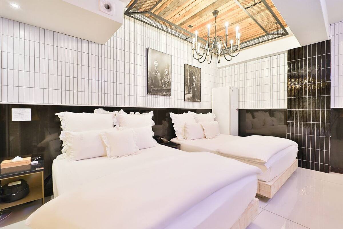 Quarto de hotel moderno com duas camas, um candelabro e paredes revestidas de azulejos.