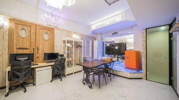 Una habitación de hotel moderna con un escritorio de madera, dos sillas de oficina, una mesa de comedor con sillas, un televisor y un letrero de neón.