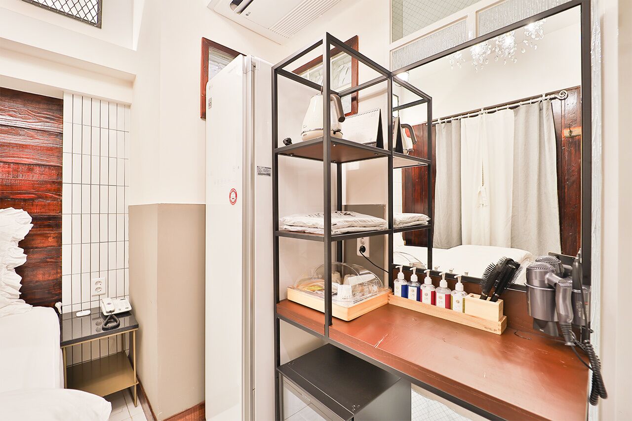 Habitación de hotel con tocador de madera, espejo, repisa con artículos de aseo y secador de pelo.