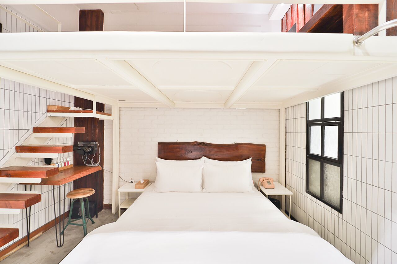 Un dormitorio con una cama grande, cabecera de madera, una mesita con un teléfono y un taburete.