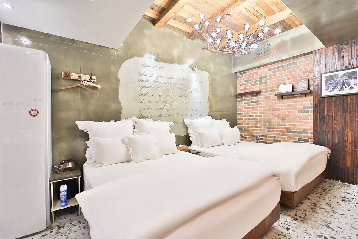 Quarto com duas camas, parede de tijolos, teto de madeira e um candelabro.