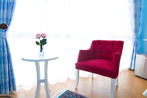 A room with a red chair, a small white table with a vase of flowers, and a patterned rug.
