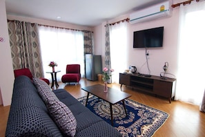 A living room with a sofa, red armchair, coffee table, and a flat-screen TV mounted on the wall.