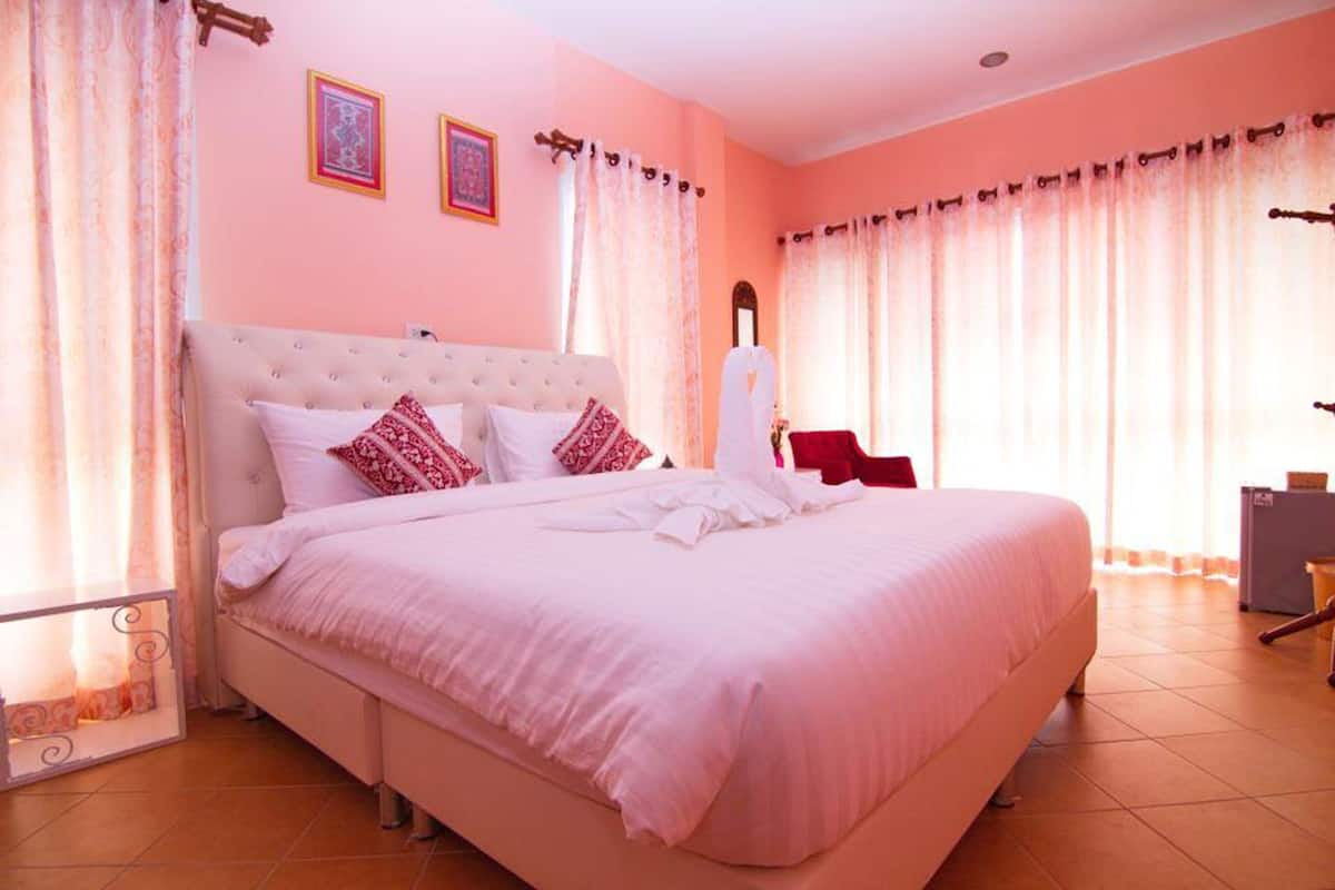 A large bed with a tufted headboard, white bedding, and red decorative pillows. There are two framed pictures on the wall above the bed.