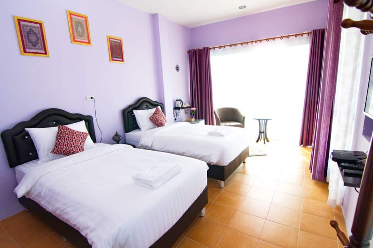 A hotel room with two beds, a chair, a small table, and a window with curtains.