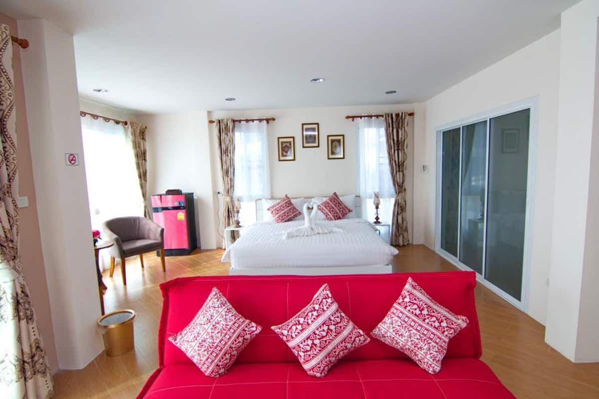 A hotel room with a large bed, a red sofa, and a sliding glass door to the outside.