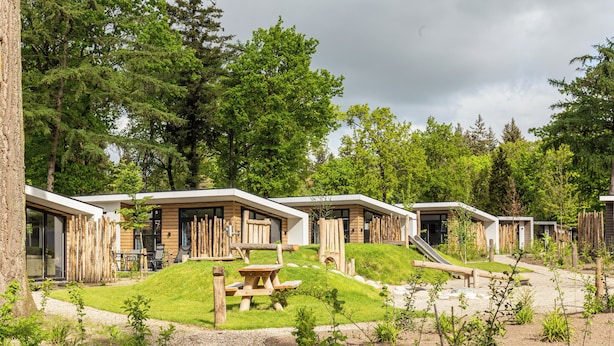 Une rangée de cabanes en bois, dotées de tables de pique-nique, entourée d’une zone boisée.