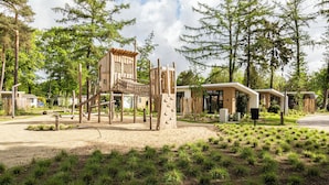 Un terrain de jeux doté de structures d’escalade et d’un bac à sable, entouré d’arbres et de bâtiments modernes.
