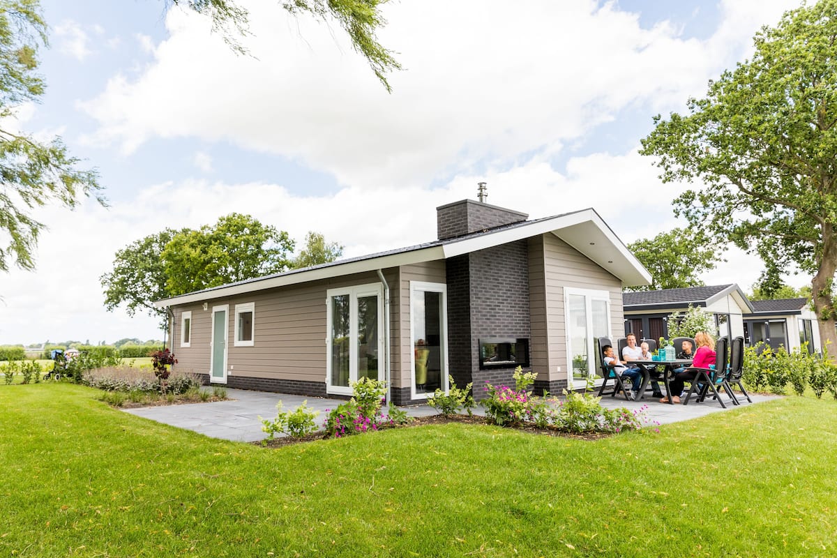 Moderni, yhden kerroksen omakotitalo, jossa on patioalue. Alueella on pöytä, jonka ääressä istuu ihmisryhmä.