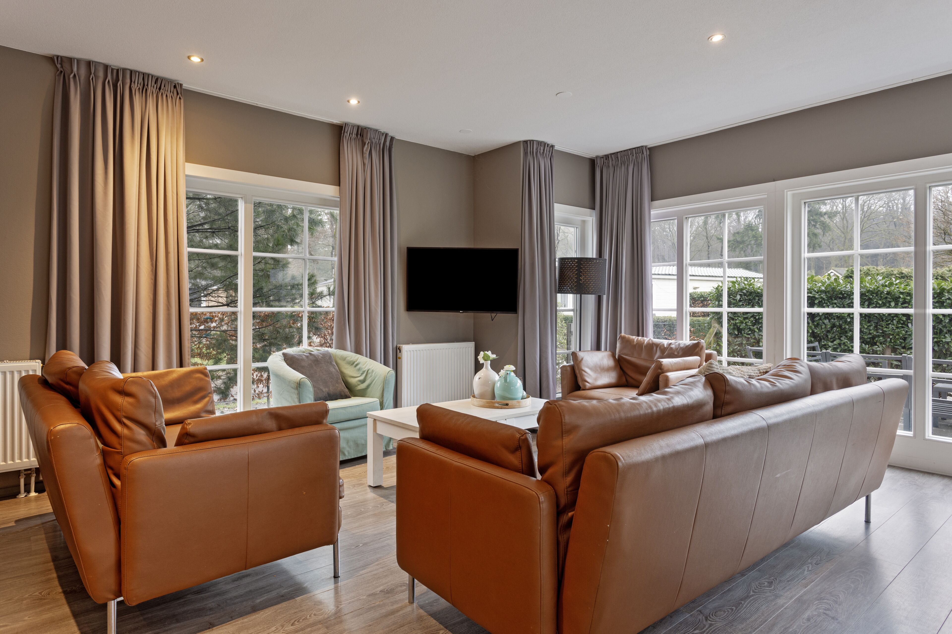 A modern living room with a brown leather sofa, a light green armchair, and a white coffee table.