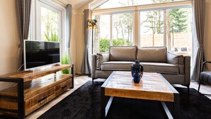 Un salon avec un téléviseur, un canapé, une table basse et de grandes fenêtres.