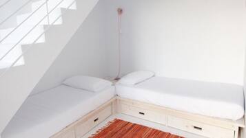 Un dormitorio moderno y minimalista con techo inclinado, una cama empotrada con cajones de almacenamiento y una alfombra roja tejida.