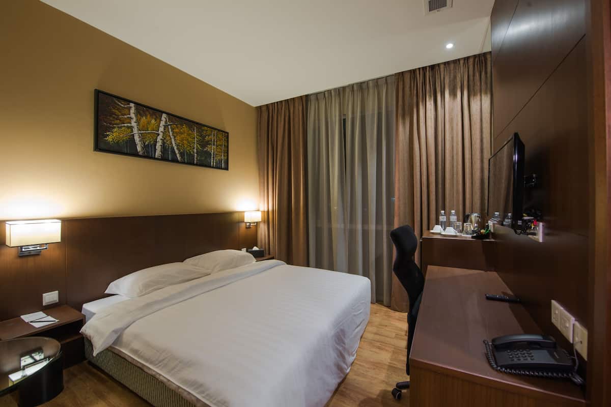 A hotel room with a large bed, two bedside tables with lamps, a desk with a telephone, and a television on the wall.