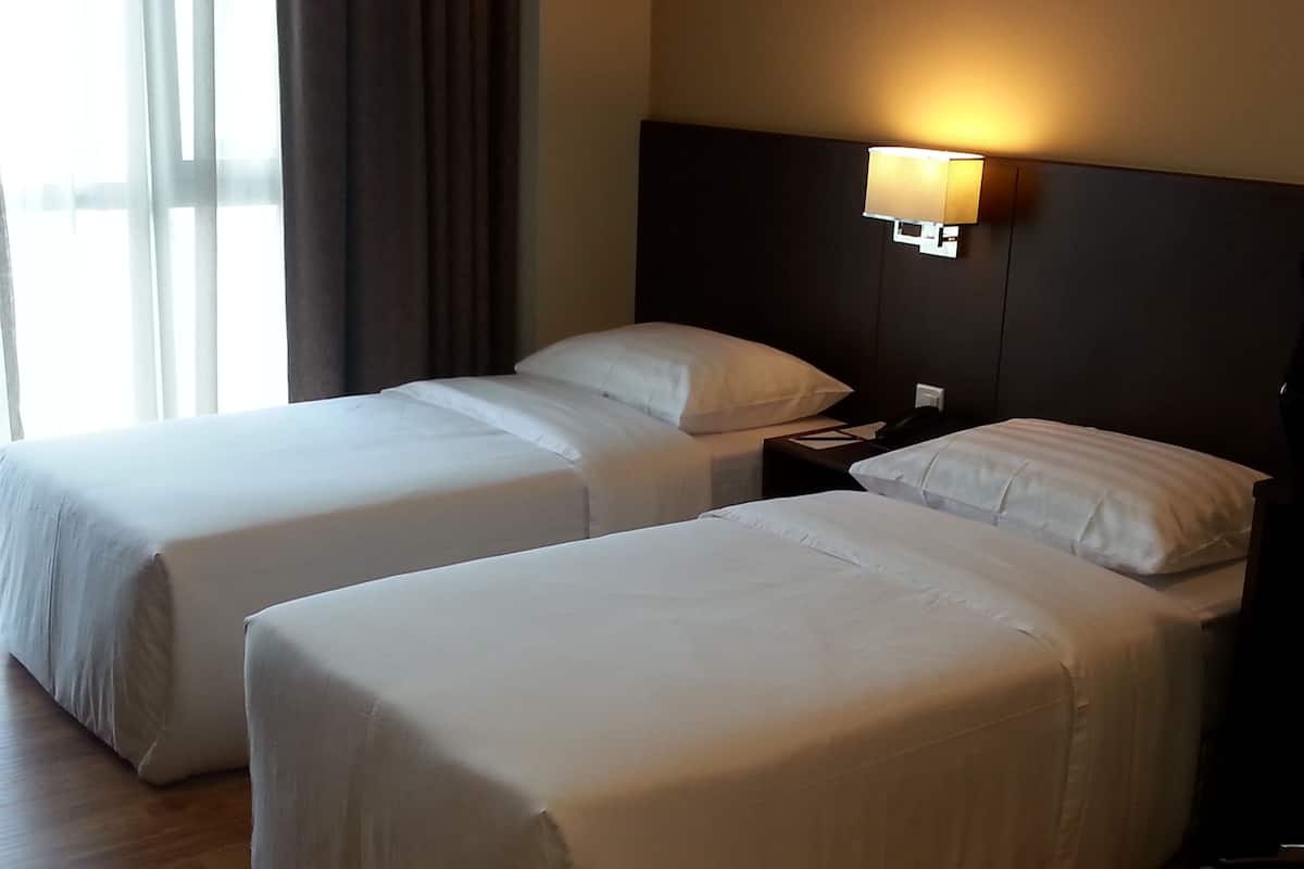 A hotel room with two single beds, a nightstand with a lamp, and a window with curtains.