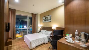 A hotel room with a bed, desk, chair, and a window with a view of a cityscape at night.