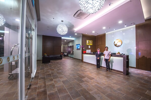 A hotel reception area with a reception desk, a seating area, and a large chandelier.