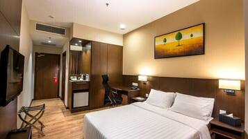 A hotel room with a bed, desk, chair, TV, and artwork on the wall.