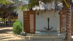 A beachside building with a thatched roof, wooden shutters, and an anchor symbol on the wall.